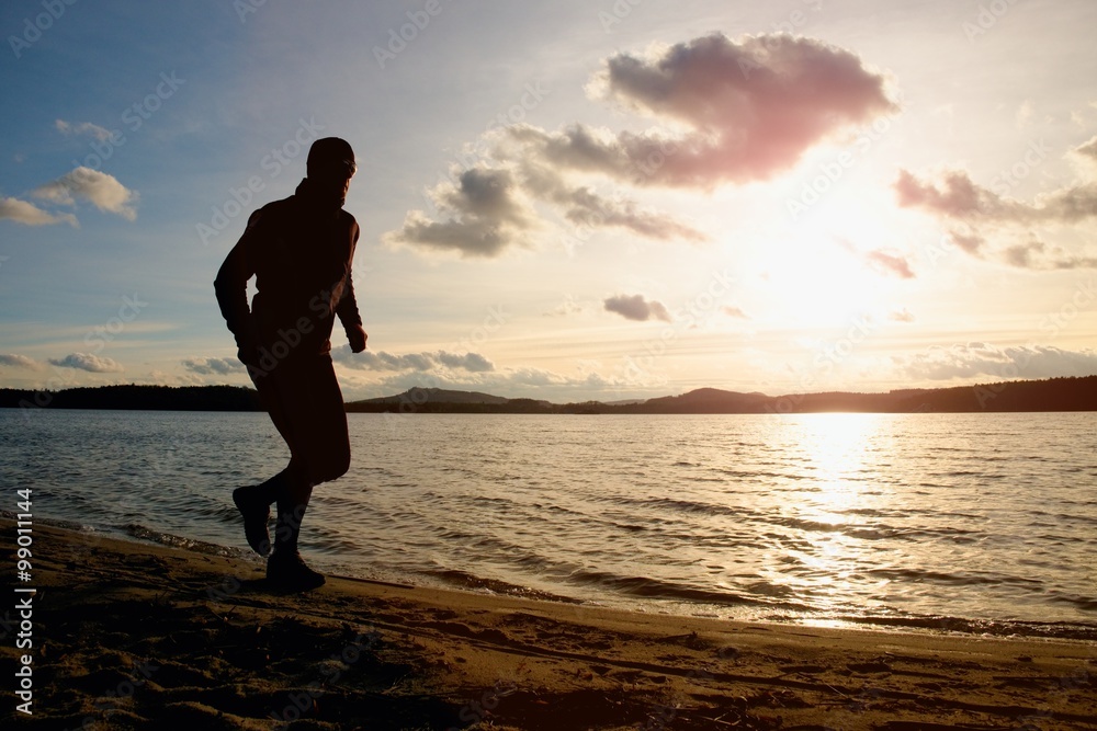 Tall man with sunglasses and dark cap is  running on beach at autumn sunset