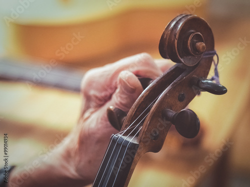 Old man luthier hands tuning aged violin

