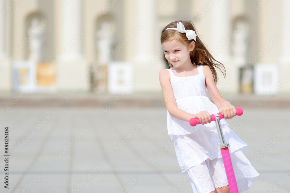 Adorable little girl riding her scooter in a summer park Adorable little girl riding her scooter in a summer park
