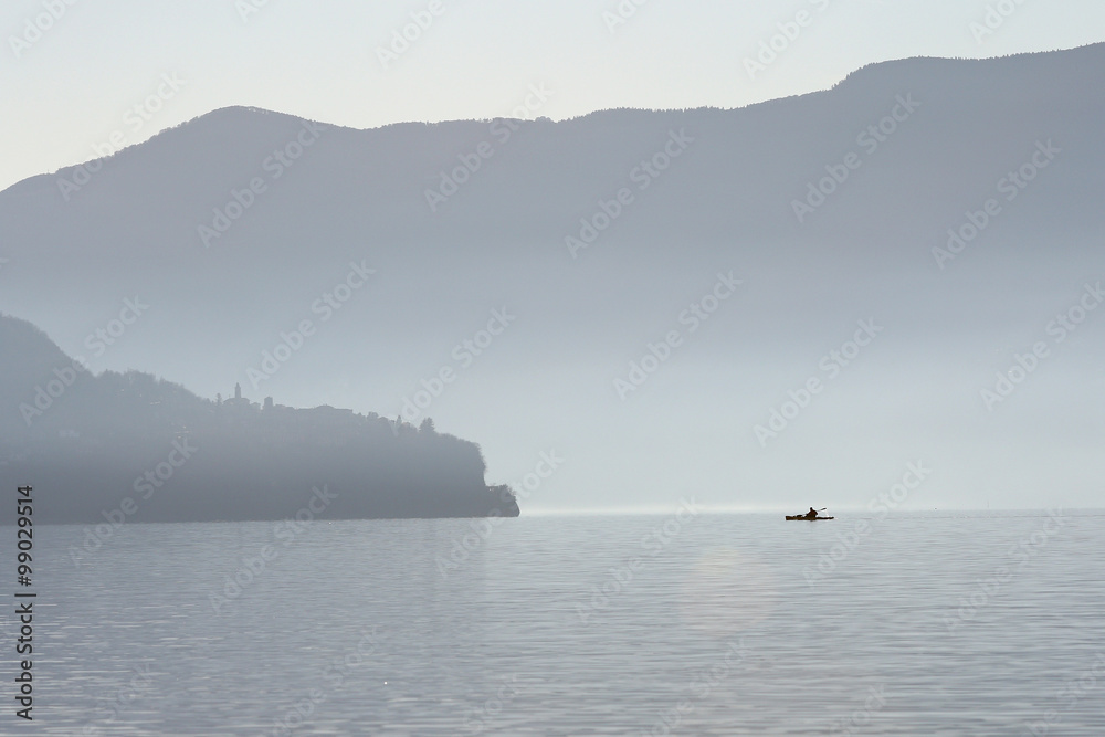 Kayak crossing lake in the mountains on a misty morning