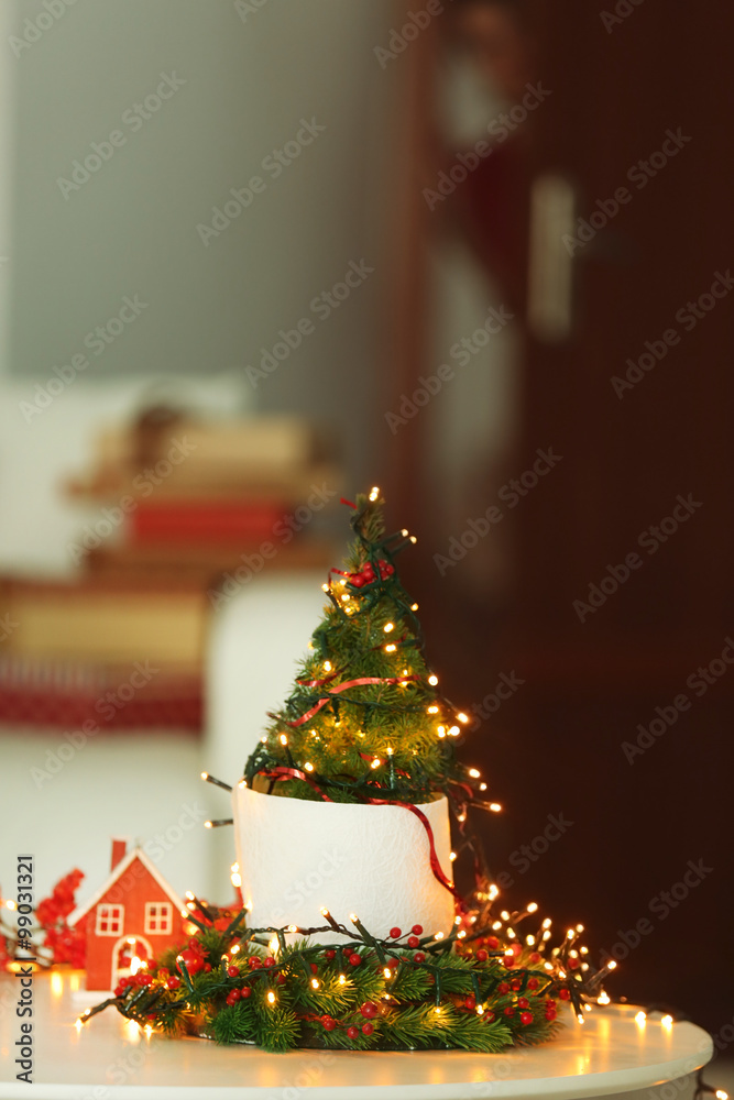 Illuminated small Christmas tree and girl standing on the background