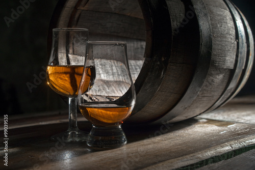 Two glasses of strong alcohol, amid oak barrels