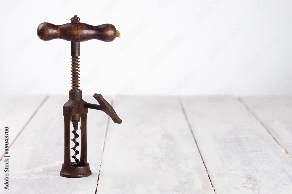 Antique corkscrew on a white painted table on white background. The corkscrew is made of rustymetal  with a wooden handle.