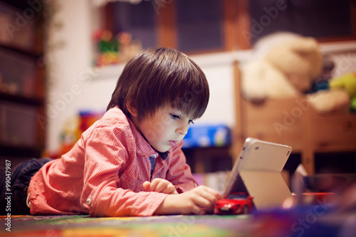 Cute little boy, lying on the floor in kids room, playing on tab