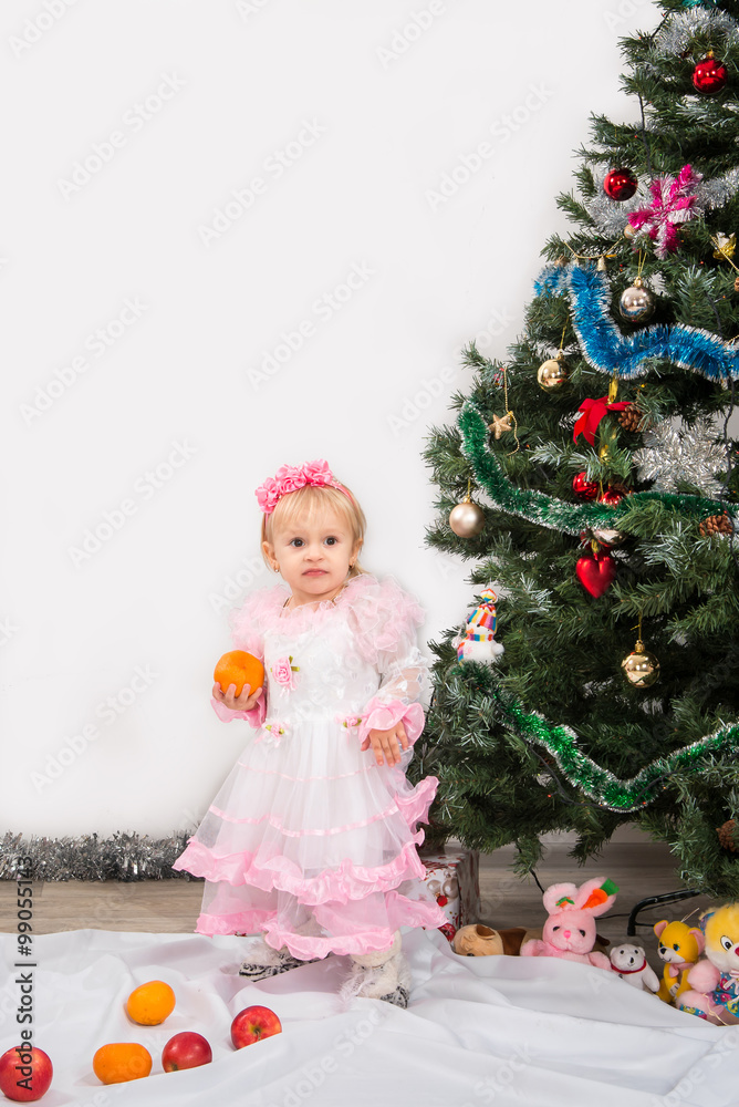 Little girl near the Christmas tree eats mandarins