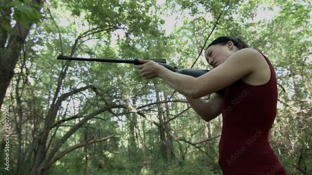 Low, side view of a young woman firing a .22 caliber rifle in woodland. Recorded in 4K, Ultra High Definition. Low, side view of a young woman firing a .22 caliber rifle in woodland. Recorded in 4K, Ultra High Definition.