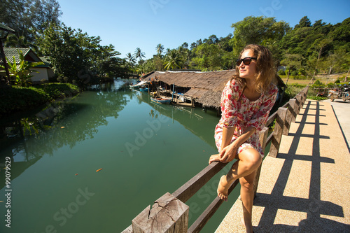 Beautiful caucasian woman sitting on the bridge over the river in the asian fishing village. © De Visu