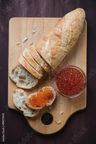 Wooden chopping board with red caviar and sliced french baguette