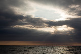 
Sun rays through dark clouds cover the sea