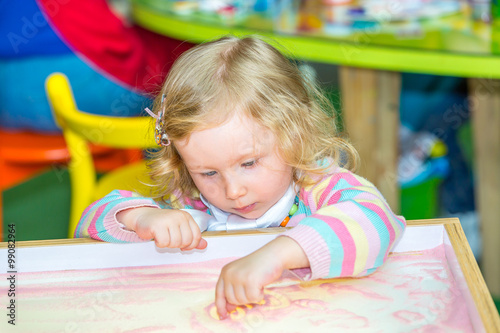 Cute child girl drawing draws developing sand in preschool at table in kindergarten by method of Montessori