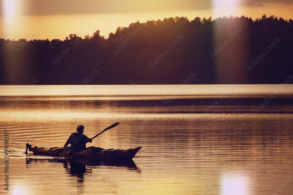 The man rowing oars in boat of kayak type on the lake at early evening. Golden sunset.Summer time, active recreation. Healthy lifestyle and care about mental health, resting in  privacy and peace.