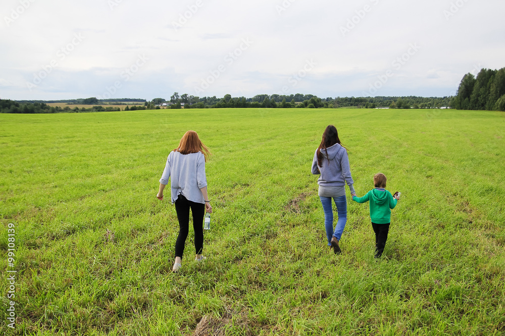 Young beautiful mother walking on the field in summer with her s Young beautiful mother walking on the field in summer with her s