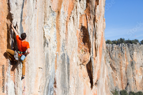 Young male climber hanging by a cliff.