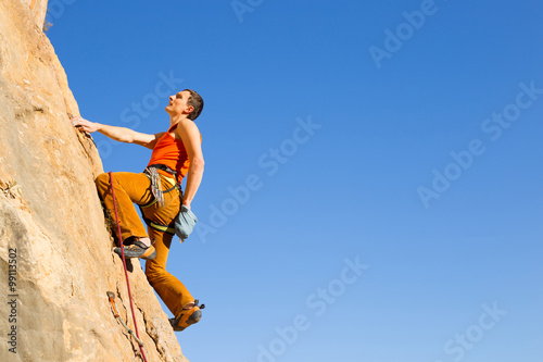 Young male climber hanging by a cliff.