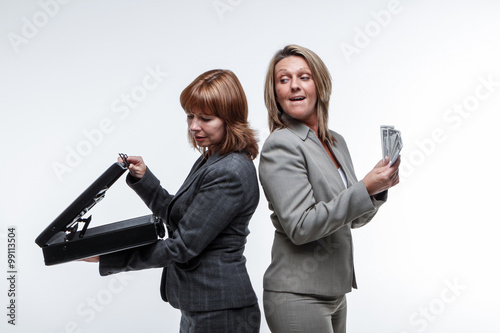 Photos Two smart suited business women exchange a briefcase for cash