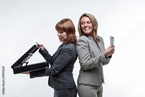 Photos Two smart suited business women exchange a briefcase for cash