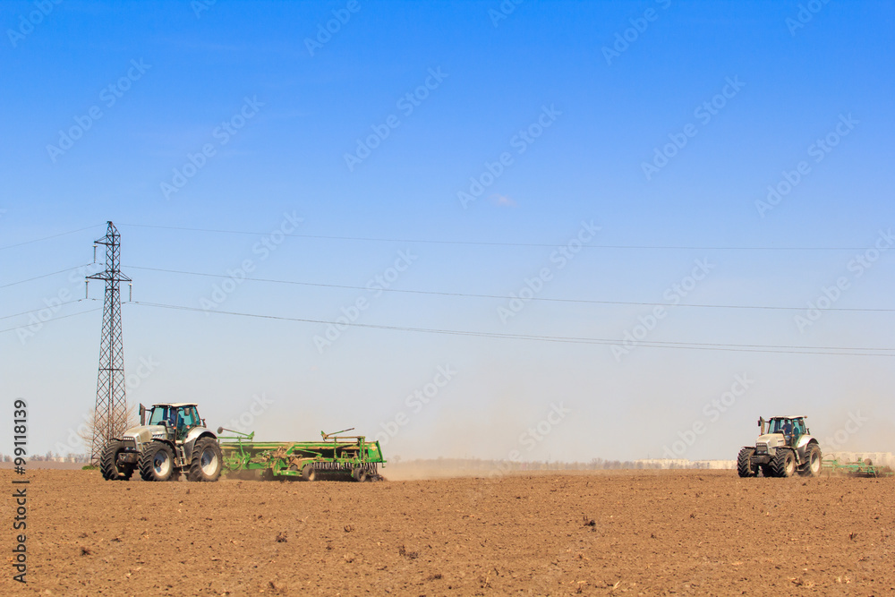 view of two tractors sowing in field in spring