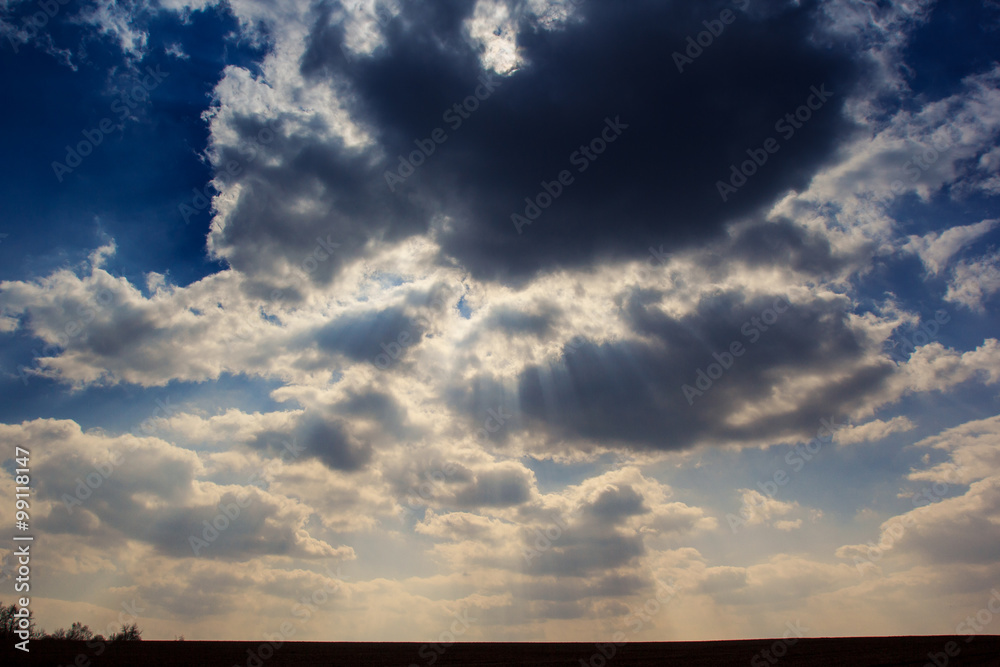 blue sky cumulus clouds above dark ploughed field in spring