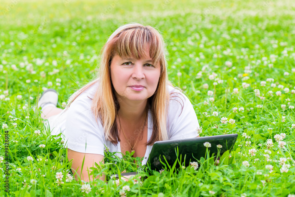 female 50 years lies with a tablet in a flower meadow female 50 years lies with a tablet in a flower meadow