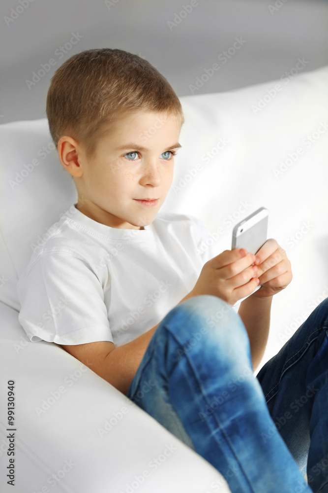 Little boy with mobile phone sitting on a sofa at home Little boy with mobile phone sitting on a sofa at home