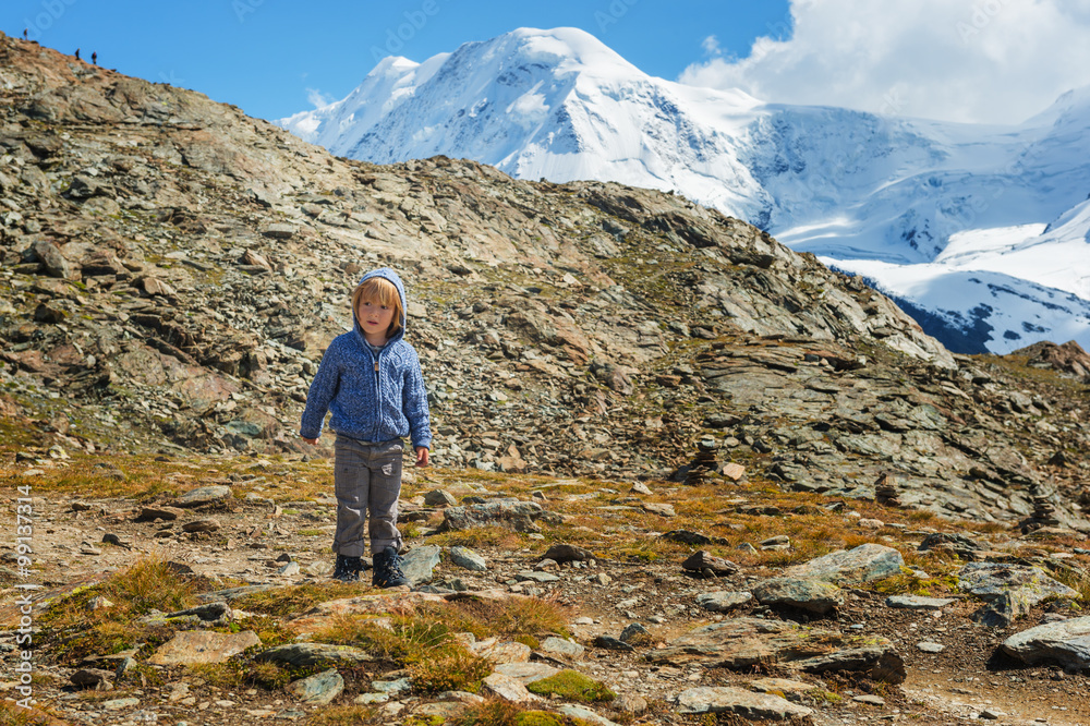 Cute kid boy resting in Alps, wearing warm knitted jacket and mountain boots