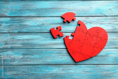 Red puzzle heart on blue wooden background photo