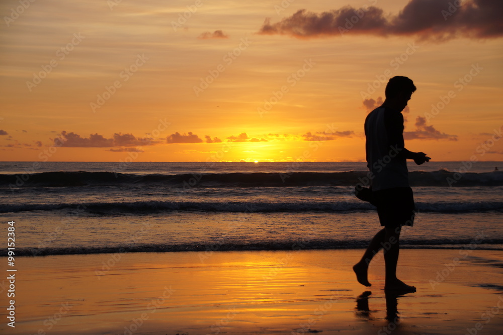 Man walking on the beach at sunset 
