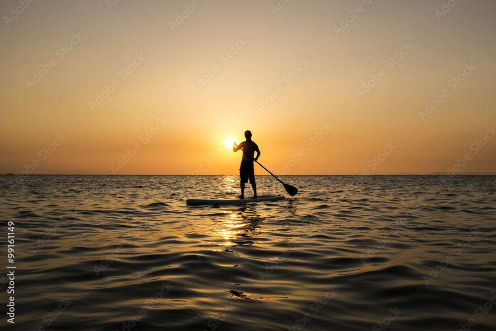 Man paddling while standing on a surfboard in the sunset, Otres Beach, Cambodia.