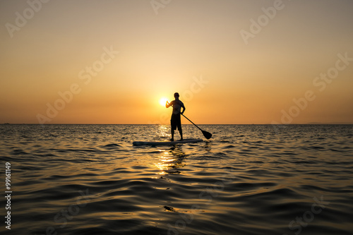 Man paddling while standing on a surfboard in the sunset, Otres Beach, Cambodia.