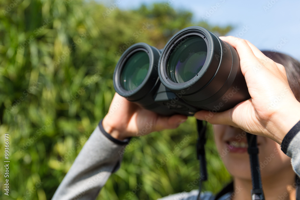 Young woman looking though binoculars at forest Young woman looking though binoculars at forest