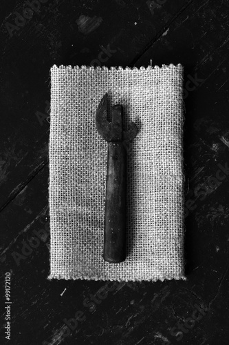 Old dirty can opener on the matting, on black boards. Top view closeup. Rustic styleThe concept of rustic kitchen. Black and white photo photo