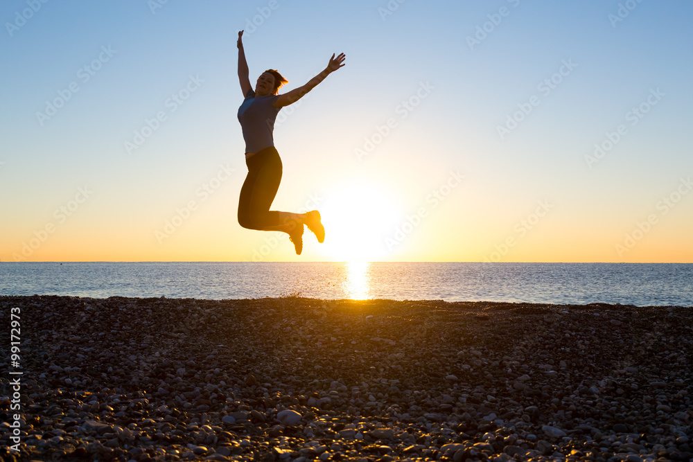 Silhouette of Happy Female jumping high with arms raised on beach sunrise