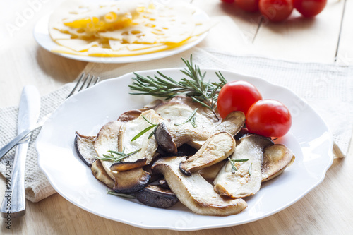 Fried eryngii mushrooms with fresh rosemary in white plate on wooden background