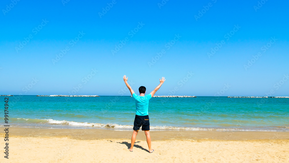 Sporty man standing by beach with arms outstretched Sporty man standing by beach with arms outstretched