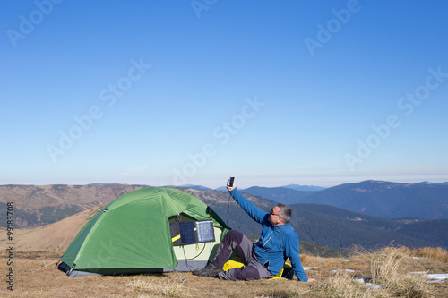 The solar panel attached to the tent. The man sitting next to mobile phone charges from the sun.