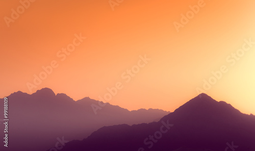 Orange and yellow sunset above layers of mountains.