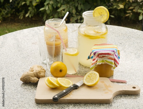 Detailed Picture of all ingredients neccesary to cook a homemade lemonade consist from water, lemon, ginger and glass of honey. Pitcher, chopping board, kitchen knife, lemon slices, glasses with straw photo