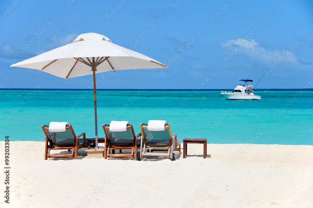 three beach chairs with white umbrella and yacht at ocean front