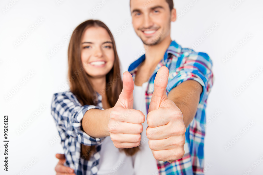 Happy cute couple in love embracing each other showing thumbs up Happy cute couple in love embracing each other showing thumbs up