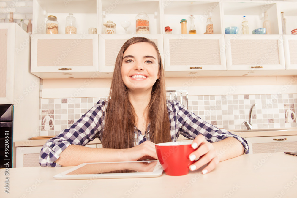 Happy girl sitting in the kitchen with tablet and a cup of coffe Happy girl sitting in the kitchen with tablet and a cup of coffe