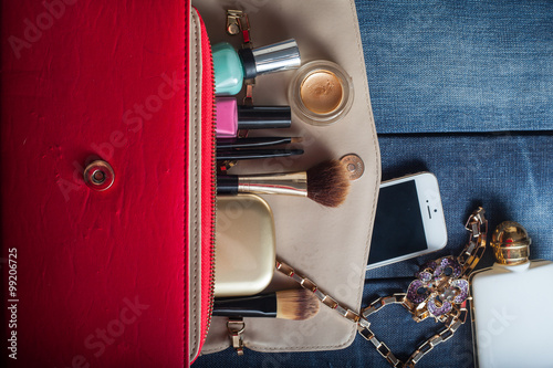 female handbag with cosmetics and mobile on jeans background