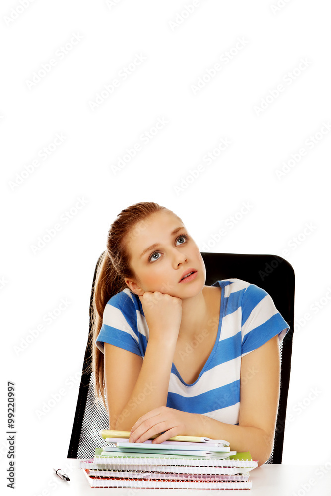 Teenage woman sitting behind the desk and thinking Teenage woman sitting behind the desk and thinking