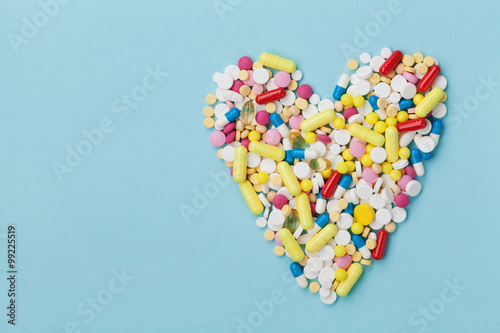 Foto Colorful drug pills in shape of heart on blue background, pharmaceutical concept
