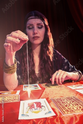 Composite image of female fortune teller using pendulum