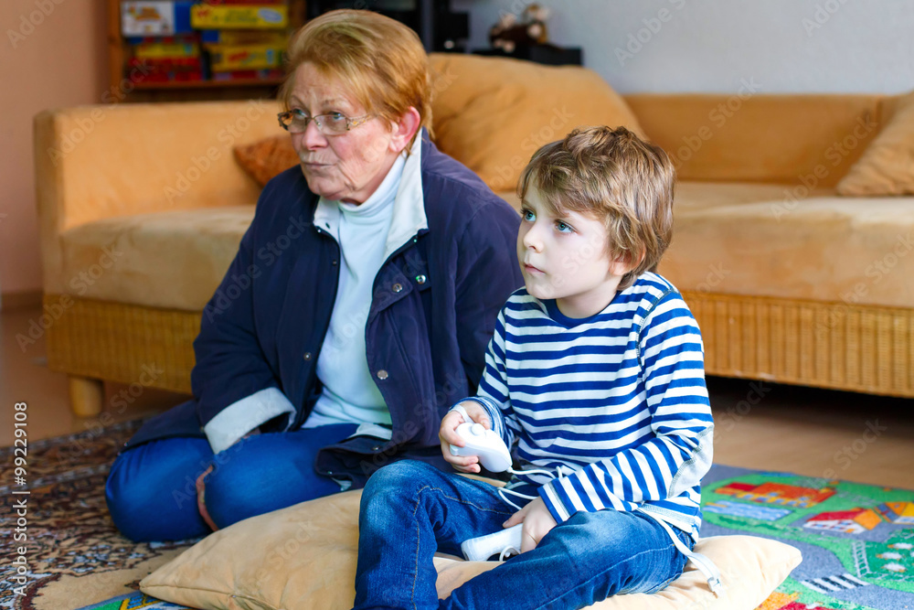 Fototapeta premium Little kid boy and grandmother playing video game console