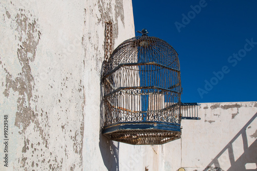 Принти на полотні Empty stylish bird cage hanging on the old wall. Bright blue sky.