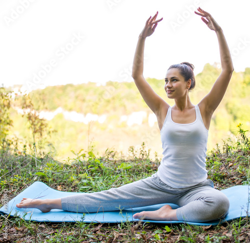 beautiful girl does exercises on a carpet in nature looking ahea photo