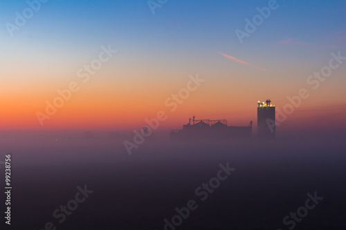 Industrial foggy landscape  silhouette of old factory against the sunset sky and the mist at blue hour at night