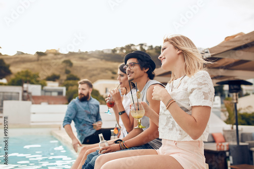 Happy young friends sitting by the pool having drinks © Jacob Lund
