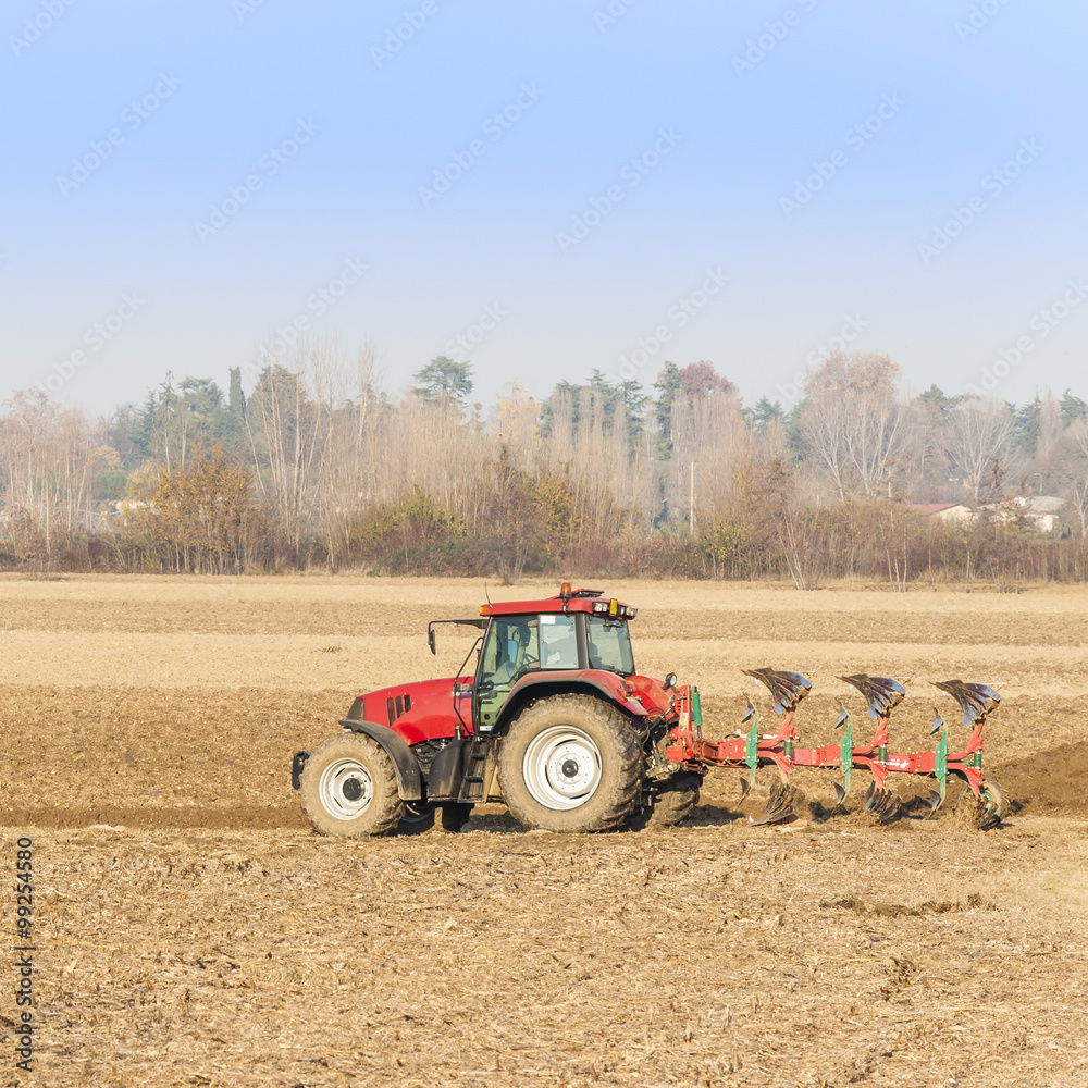 Obraz premium Red Tractor Plowing in Autumn.